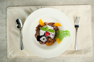 Gourmet dessert on a plate, featuring a brownie base, ice cream, fruits, and mint leaves, a culinary delight