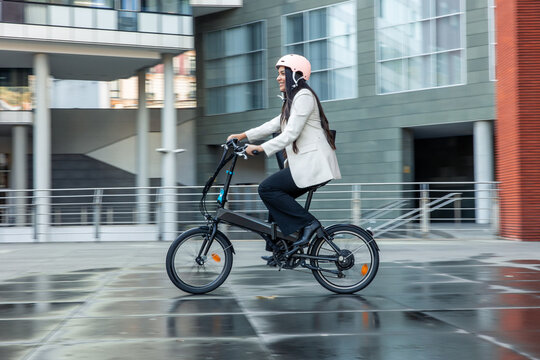 Latin businesswoman riding electric folding bike commuting to work