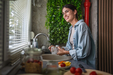Woman washing dishes at kitchen sink, doing housework