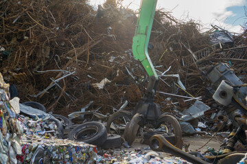 a massive pile of tangled scrap metal, rusted rebar, and wires with a green industrial grapple claw in the foreground concept of metal recycling, waste processing, heavy industry