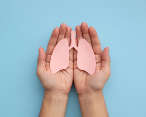 Caring hands gently cradle a delicate paper lung cutout, symbolizing health awareness and respiratory well-being on a serene blue backdrop.