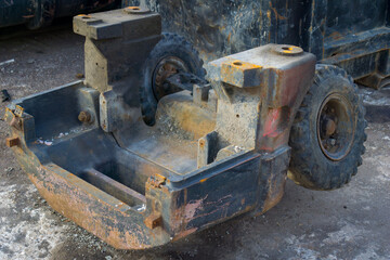 Close-up of a rusty and damaged industrial machine chassis with worn rubber wheels, abandoned in a scrapyard for metal recycling or repair.