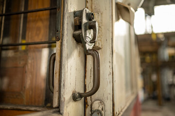 Close-up of an old tram door handle and lock mechanism with worn paint and vintage details. Historic public transport element with rustic, nostalgic atmosphere.