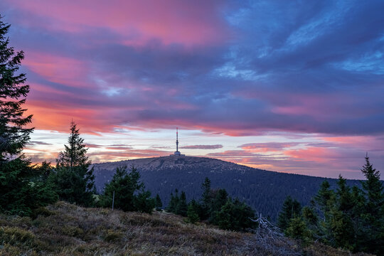 Colorful sunset over Praděd mountain in Jesen&iacute;ky, Czech Republic, with the iconic TV tower on the summit and dramatic clouds above forested hills.