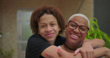 Obraz premium Teen son showing love to mother with a kiss on the cheek, both sharing a warm hug outdoors, showcasing family affection, deep bond, and emotional connection