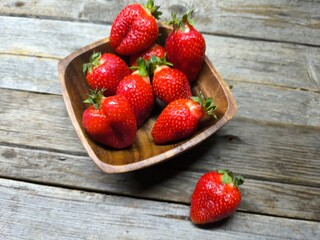 Ripe sweet strawberries in a wooden plate on a wooden