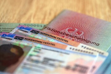 Obraz premium German Permanent resident card and document specimen lies on wooden table close up. Aufenthaltstitel and Fiktionsbescheinigung