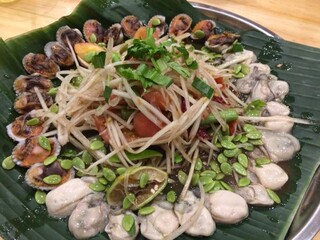 Thai local food, Thai papaya salad with mussels, oysters, lime, and herbs—served on banana leaf with vibrant shellfish and fresh vegetables in circular layout