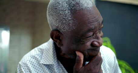 Elderly African American man resting his chin on his hand, showing concern and regret, reflecting...