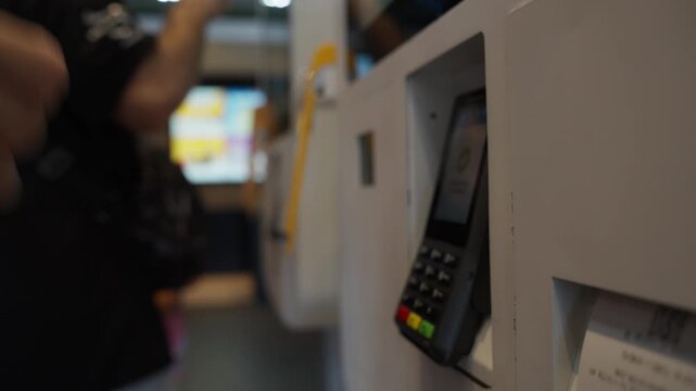 Woman taking printed receipt from self-service checkout terminal at fast-food restaurant, with pos machine appearing in background