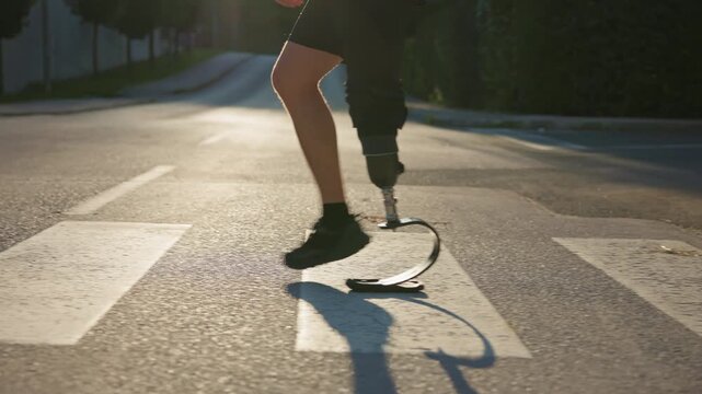 Confident stride walk of a man wearing an artificial leg, an orthopedic prosthesis, going across the street on a zebra crossing, side view close up.