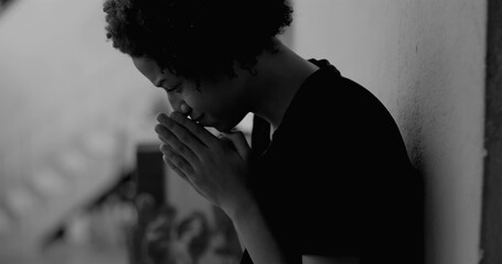 African American boy leaning against a wall, covering his face with hands, overwhelmed with sadness...