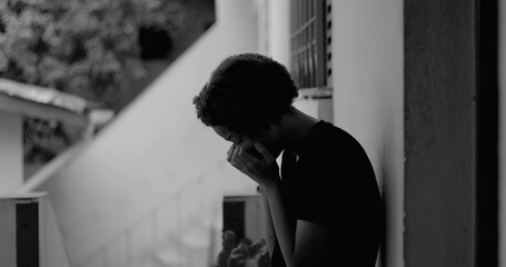 African American boy standing alone by a wall, head bowed in sadness and despair, representing...
