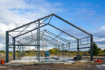 Steel structure frame of industrial warehouse under construction on site during sunny autumn day