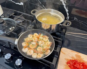 Shrimps and pasta cooking on stove, tomatoes on countertop in kitchen