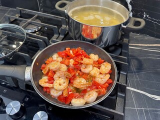 Cooking shrimps with tomatoes and pasta on stove in kitchen, closeup