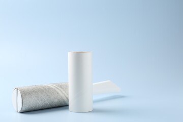 Lint roller with used sticky tape and new adhesive roll on light blue background, closeup. Space for text