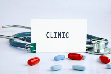 A clear sign reading clinic stands out amidst scattered red and blue pills and a stethoscope,...