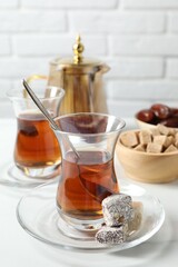 Tasty Turkish tea in glass cups, brown sugar and sweets on white marble table, closeup