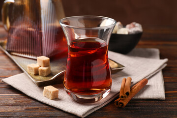 Tasty Turkish tea in glass cup, brown sugar, cinnamon, sweets and teapot on wooden table, closeup