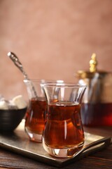 Tasty Turkish tea in glass cups, sweets and teapot on wooden table against brown background, closeup