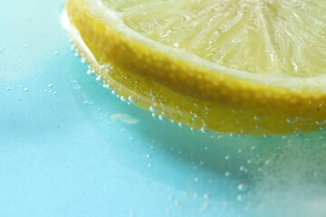 Slice of lemon in soda water on light background, closeup