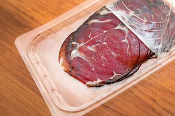 Thin slices of smoked red meat in opened vacuum packaging on table, ideal for food photography and product presentation