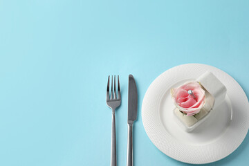 Beautiful table setting for romantic dinner, box with engagement ring and rose on light blue background, above view. Space for text
