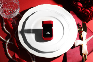 Beautiful table setting for romantic dinner, box with engagement ring and roses on red background