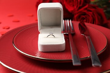 Beautiful table setting for romantic dinner, box with engagement ring and roses on red background,...