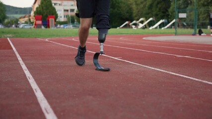 Man with disability wearing a prosthetic running blade on an athletic track, pausing to tie a shoelace, slow motion. Determination and resilience concept.