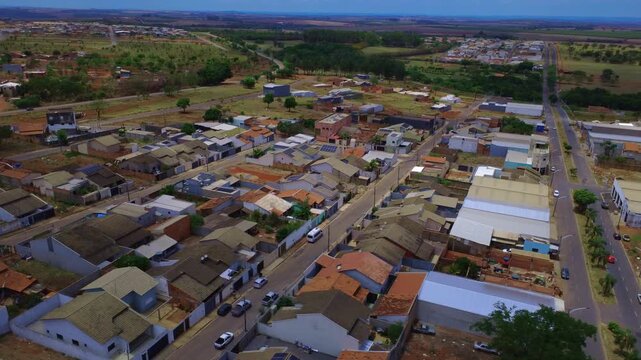 Sobrevoo de drone 4K mostrando casas, telhados e ruas em cidade do interior no Brasil, dia ensolarado.