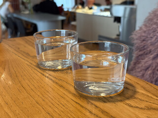 Two glasses of water on wooden cafe table. Simplicity, hydration, and calm atmosphere in social dining environment.
