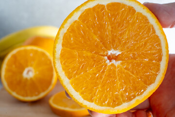Fresh ripe orange cut in half showing juicy citrus segments held in hands with banana in background. Healthy vitamin C rich fruit and natural nutrition for wellness and immune system support concept.