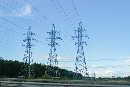 High power transmission towers with power lines against a clear blue sky. Electricity supply infrastructure for energy concept.