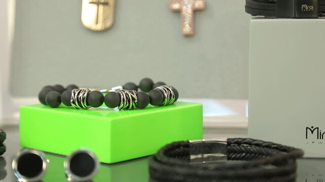 Stylish men's jewelry display features black braided leather bracelets, matte beaded bracelets, and contemporary silver cufflinks. Ideal for fashion and luxury retail settings.