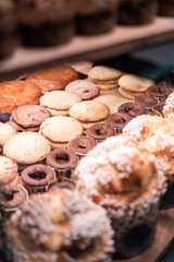 A tempting display of fresh pastries, including various cookies, chocolate fondants, and muffins, in a bakery showcase. A concept of sweet indulgence and the daily treats of a local cafe.