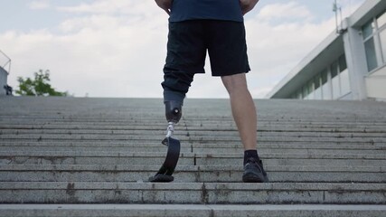 Man in sportswear wearing a prosthetic sports foot standing with his hands on waist at the bottom of an outdoor staircase, rear view. Win, challenge, and goal concepts. - Powered by Adobe