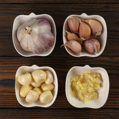 Different Stages of Garlic Preparation: Whole, Cloves, Peeled, and Minced in Ceramic Bowls on Wooden Table