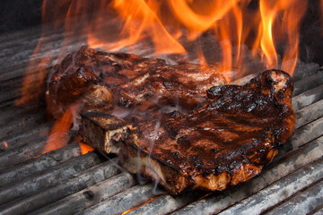 Juicy grilled steak with rosemary and pepper on fire, BBQ meat cooking over open flame.
