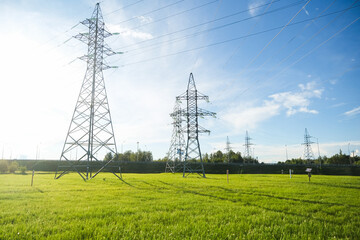 Power lines and metal pylon in sunny green grass field with blue sky. Concept of electrical energy, infrastructure, and industrial landscape.