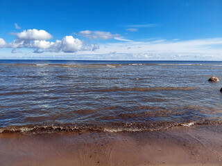 Gentle waves of the Sea wash onto a sandy beach on a sunny day with a blue sky