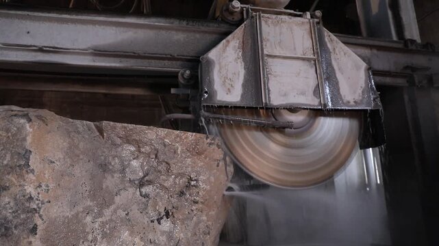 Close-up of a large diamond saw cutting a natural stone block in a factory. Water cools the blade and suppresses dust during the industrial marble or granite processing.

