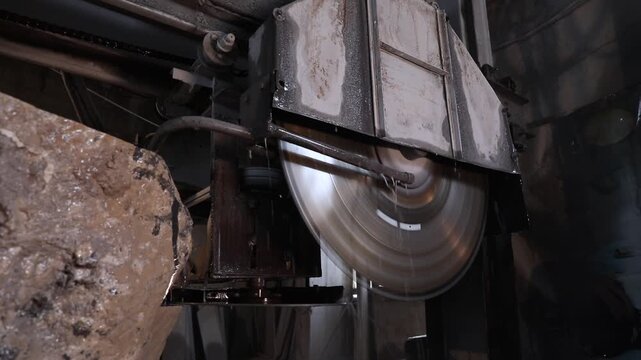 Close-up of a large diamond saw cutting a natural stone block in a factory. Water cools the blade and suppresses dust during the industrial marble or granite processing.

