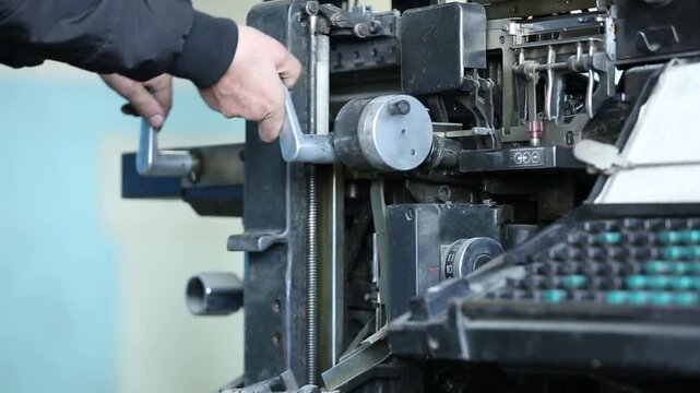 Skilled worker adjusts and maintains complex vintage printing press or typesetting machine. Detailed close-up of hands on intricate industrial components and levers.