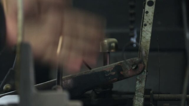 Skilled worker adjusts and maintains complex vintage printing press or typesetting machine. Detailed close-up of hands on intricate industrial components and levers.