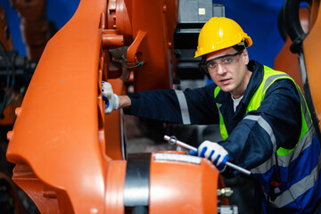 Two factory engineers wearing safety gear checking documents in front of robotic arms. Concept of...