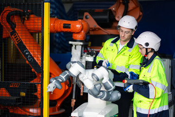 Engineers in safety uniforms inspecting robotic arm machinery in a factory. Concept of industrial automation, teamwork, manufacturing process, and engineering technology in modern industry.