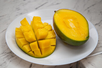 Fresh mango fruits, prepared in a hedgehog style, cubes and pieces on a white plate, isolated on a white background. Organic food. Vegetarian.