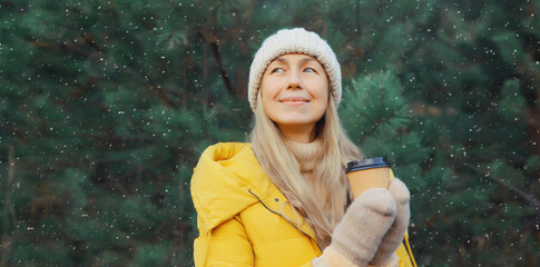 Winter day, happy smiling woman holding cup of coffee drink enjoys snow, against Christmas tree